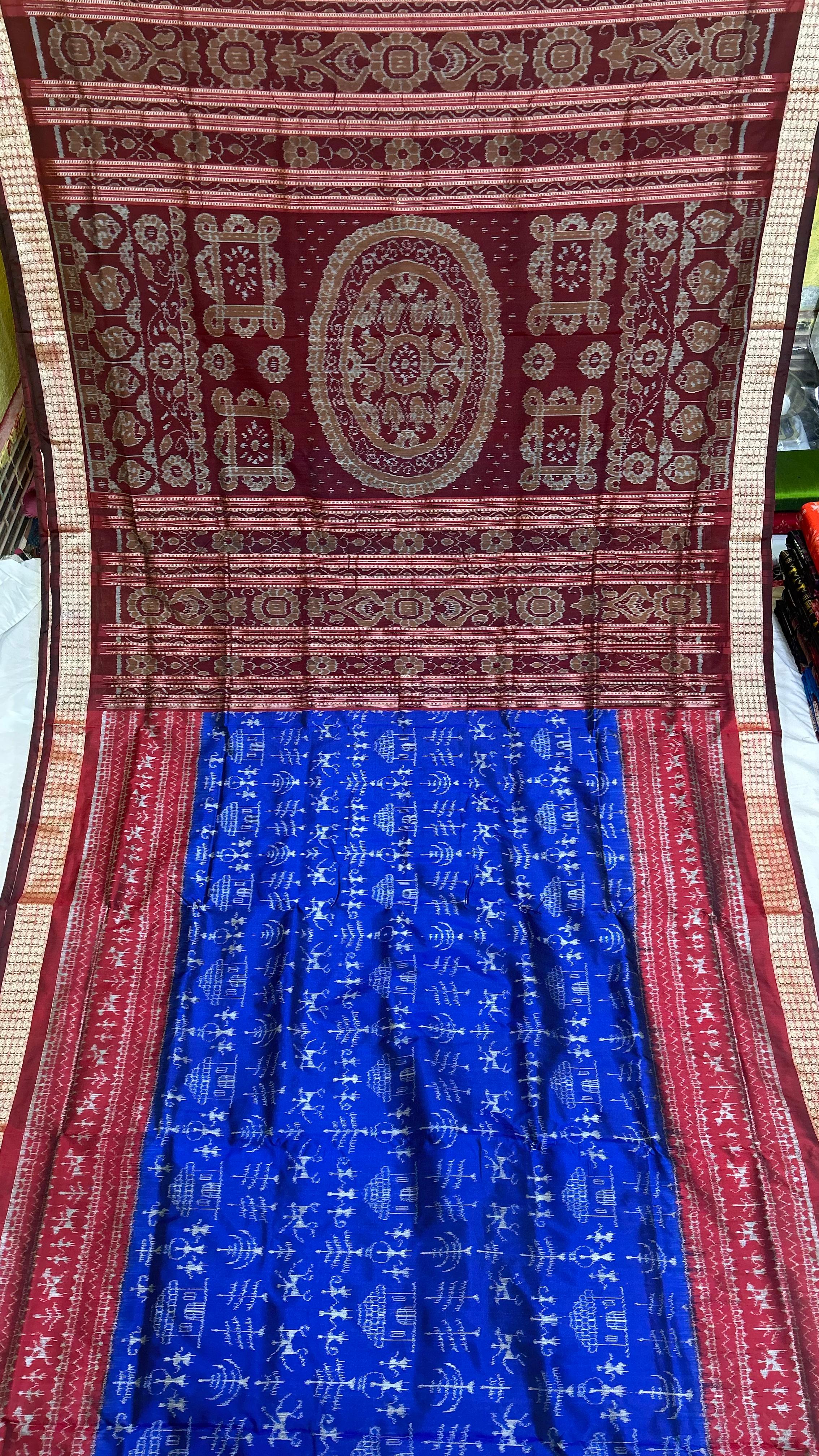 A blue and maroon silk saree featuring body patterns of men, flowers, temples, and a pallu adorned with big flower designs.