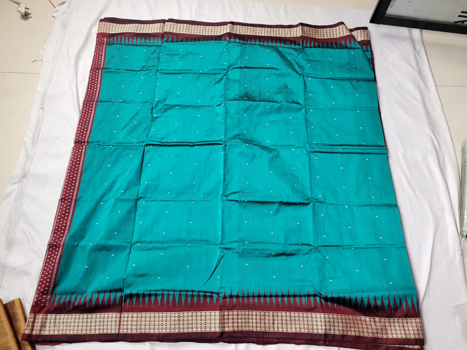 The sapphire green and maroon color silk pata saree has a beautiful body pattern with intricate floral designs on the pallu, adding elegance.