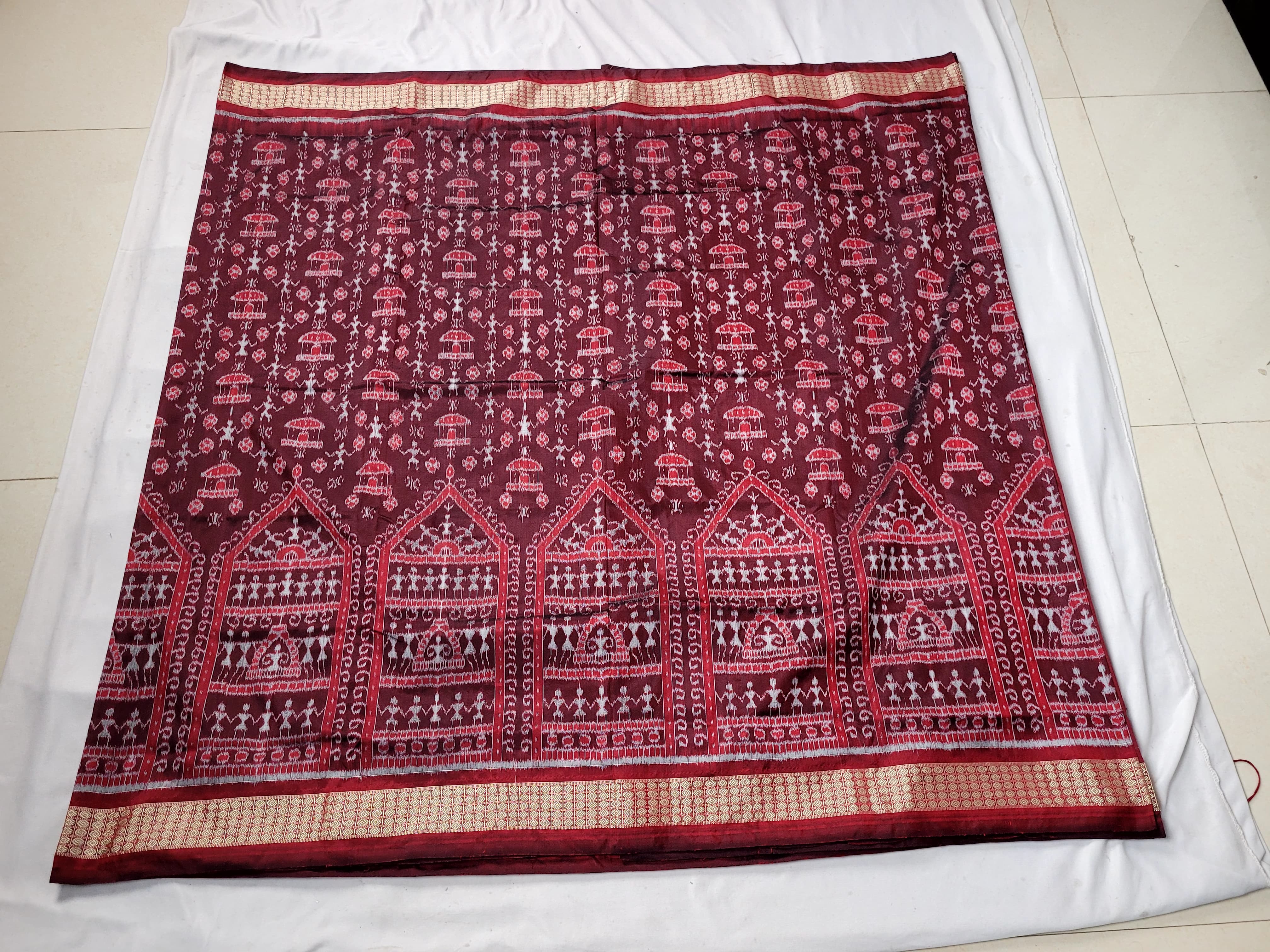 The brown and maroon pata saree showcases a body pattern of little men and houses, with a pallu design featuring large flowers.