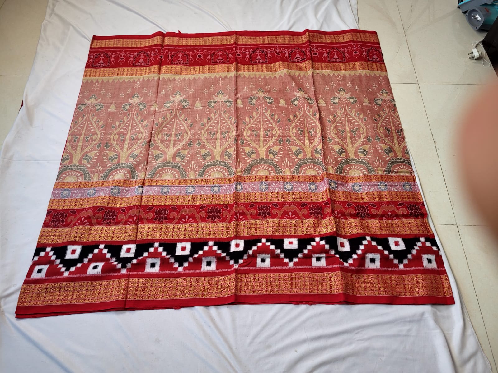 The gray and red Sambalpuri cotton saree features a floral tree border with Pasapali design, complemented by a pallu adorned with big flowers.